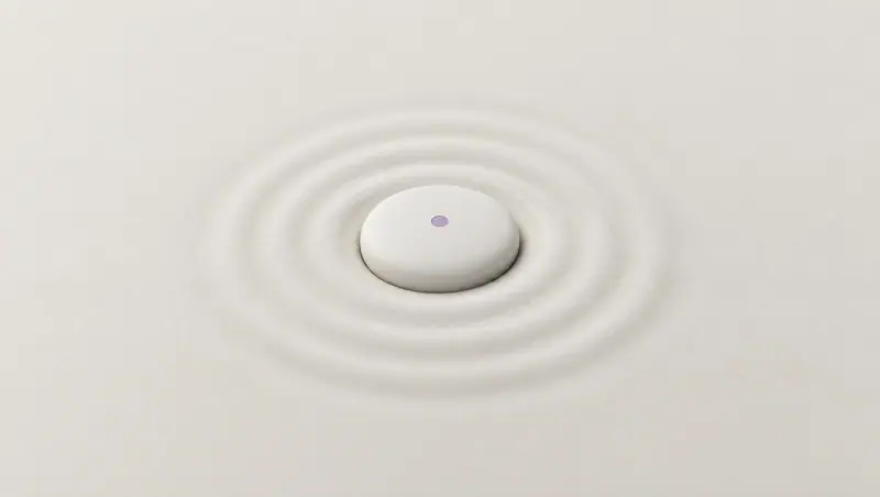 A soft white button pressed into a cushioned surface, with fine ripples spreading outward and a lavender dot at its centre.